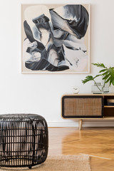 Stylish scandinavian living room interior with modern wooden commode, black rattan basket, tropical leaf in vase and elegant personal accessories. Mock up paintings on the white wall. Template. 