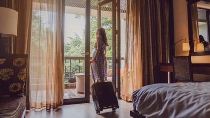Asian women are staying in a hotel room with luggage.Open the curtain and  door in the room looking to outside view.Travel in holidays concept.Vintage tone. - obrazy, fototapety, plakaty