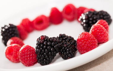 raspberries and blackberries laid out on a white plate in circle