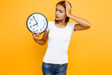 Portrait of a shocked girl holding a watch, girl overslept in the morning, on a yellow background