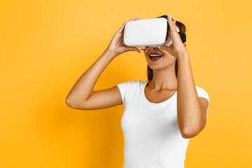 Young beautiful girl in virtual reality glasses on yellow background