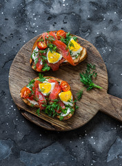 Smoked salmon Nicoise toasts on rustic wooden board on dark background, top view