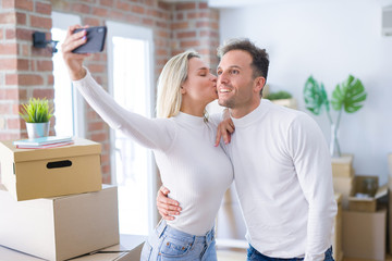 Young beautiful couple standing using smartphone to take selfie kissing at new home around cardboard boxes