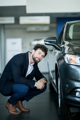 Young man looking at wheels at his new car in salon