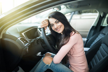 Portrait of beautiful young woman sitting in a new car and smiling in showroom