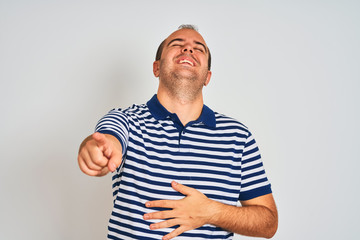 Young man wearing casual striped polo standing over isolated white background laughing at you, pointing finger to the camera with hand over body, shame expression