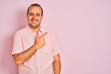 Young man wearing elegant shirt standing over isolated pink background cheerful with a smile of face pointing with hand and finger up to the side with happy and natural expression on face