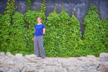Girl on the wall background of green leaves, copy space. A stone floor, a wall of creeper and a...