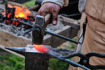 Hammer blow on hot workpiece is in the grip of blacksmith. Brazier, red-hot billet and blacksmith's hand with a sledgehammer. The process of forging iron in the open air.