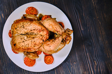 Festive dinner with meat bird. Fried chicken with golden crust on dark wooden background. Big whole grilled chicken on a plate, copy space.