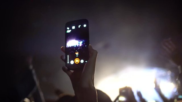 Concert at night, people raise their hands, take pictures on smartphone,