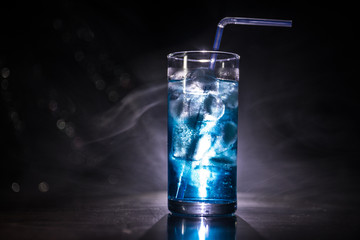 Cocktail glass splashing on dark toned smoky background or colorful cocktail in glass. Party club entertainment. Mixed light.