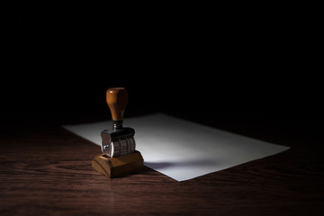Close up view of rubber date stamper on wooden table with dark toned foggy background.