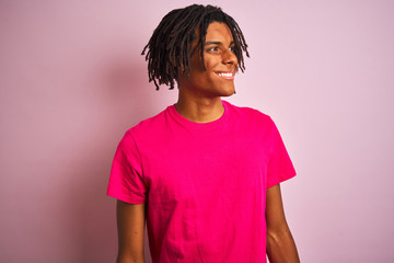 Fototapeta premium Afro american man with dreadlocks wearing t-shirt standing over isolated pink background looking away to side with smile on face, natural expression