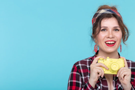 Portrait of a pretty young positive woman in a plaid shirt holding a yellow film vintage camera posing on a blue background with copyspace. Concept lovers of photography and shooting.