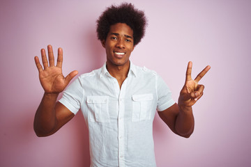 Young american man with afro hair wearing white shirt standing over isolated pink background showing and pointing up with fingers number seven while smiling confident and happy.