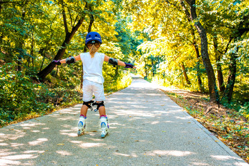 Back view of little girl wearing protection pads and safety helmet enjoying inline roller skating...