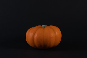 A mini orange pumpkin on a black table. Autumn is pumpkin time. Black background. Space for text.