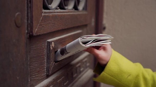 Close-up of person hand removing newspaper from mailbox at wooden door of a residential building
