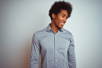 Obraz premium Young african american man with afro hair wearing grey shirt over isolated white background looking away to side with smile on face, natural expression. Laughing confident.