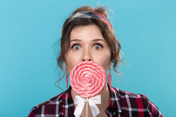 Charming young woman in retro clothes holding colorful lollipops in her hands and licking one...
