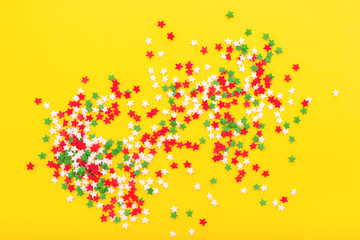 Colorful festive stars sprinkles as a frame on yellow background. Flat lay style. Top view.