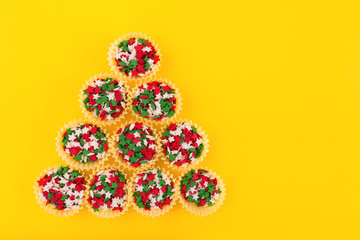 Colorful sprinkles on a yellow background making a shape of a Christmas tree. Flat lay style. Top view. Place for design.