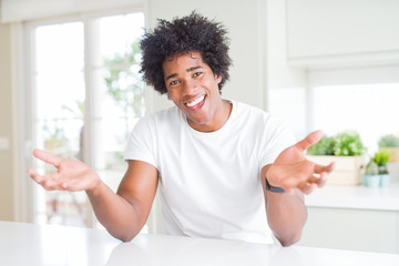 Fototapeta na wymiar Young african american man wearing casual white t-shirt sitting at home smiling cheerful with open arms as friendly welcome, positive and confident greetings