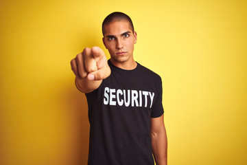 Young safeguard man with security t-shirt over yellow isolated background pointing with finger to...