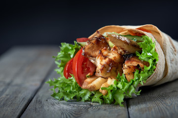 Shawarma rolled in lavash, moist grilled meat with onion, herbs and vegetables on wooden background.