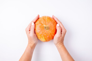 Woman hands holding a small orange pumpkin on white background. Top view.