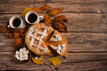 Autumn composition. Delicious homemade Apple pie, two mugs of tea, sugar cubes and autumn leaves on a wooden background.