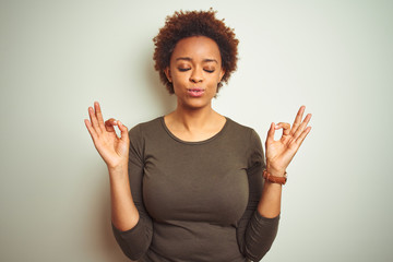 Young beautiful african american woman with afro hair over isolated background relax and smiling with eyes closed doing meditation gesture with fingers. Yoga concept.