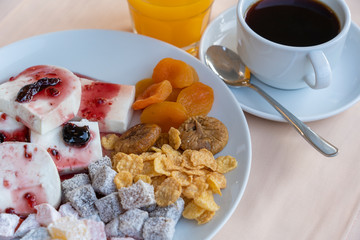 Curd cheese poured fruit yogurt, dried apricots, figs, cornflakes and cup coffee on table. Breakfast concept.