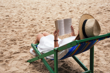 A beautiful woman lying down and reading book on the beach chair with feeling relaxed