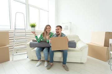 Cheerful joyful young couple charming girl and handsome man holding a box with things and a pot with a plant while moving to a new apartment. Housewarming and mortgage concept.