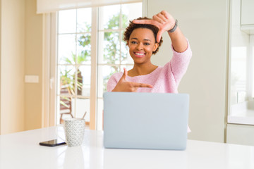 Young african american woman working using computer laptop smiling making frame with hands and fingers with happy face. Creativity and photography concept.
