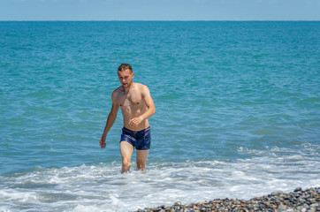 Fototapeta na wymiar Beautiful sexy man comes out of the sea on a pebble beach on a Sunny day