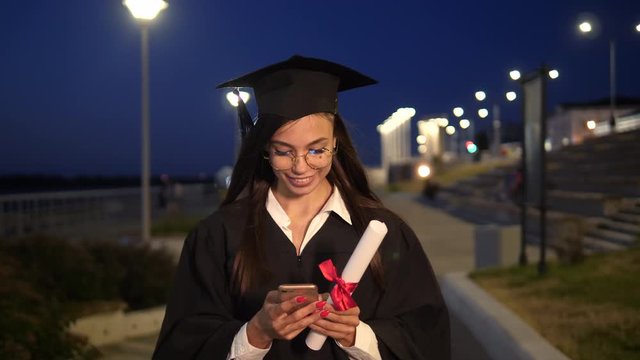 Highschool graduate girl after graduation caremony walking and texting message on the mobile phone.