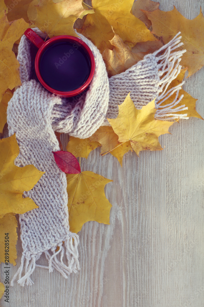 Wall mural cup of black coffee in a light scarf with autumn leaves on a wooden table top view. warming still life