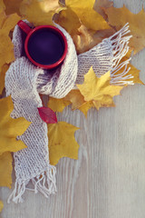 cup of black coffee in a light scarf with autumn leaves on a wooden table top view. warming still life