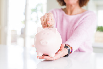 Obraz na płótnie Canvas Close up of senior woman putting a coin inside piggy bank as savings