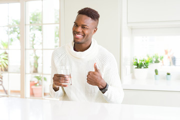 African american man driking a fresh glass of water happy with big smile doing ok sign, thumb up with fingers, excellent sign