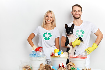 young active ambitious volunteers taking care of animals and nature, young couple holding a dog and posing to the camera while standing behind the recycling bins