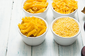 uncooked pasta variations and flour in paper bag, on white wooden table