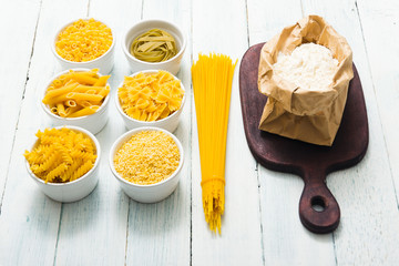 uncooked pasta variations and flour in paper bag, on white wooden table