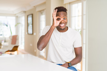 Fototapeta premium Handsome african american man on white table at home doing ok gesture with hand smiling, eye looking through fingers with happy face.