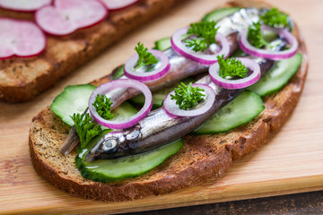 sandwich with salted small fish capelin sardines fresh cucumber parsley red onion on rye bread close up