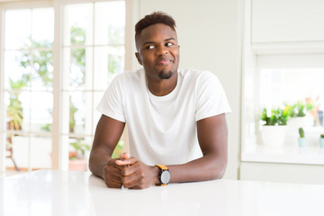 Handsome african american man on white table at home smiling looking side and staring away thinking.