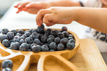 baby boy hands touch and take raw fresh blueberries indoor. baby exploring fruit